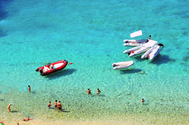 Spiaggia con persone e gommoni in mare cristallino.