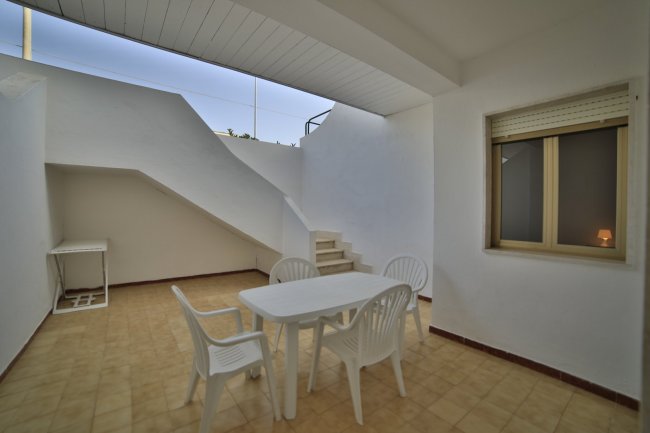 Patio con tavolo e sedie bianche, scale sul fondo.