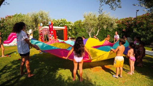 Bambini giocano all'aperto con un telo colorato.