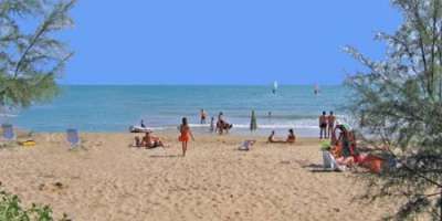 Spiaggia sabbiosa con persone che si rilassano e nuotano.