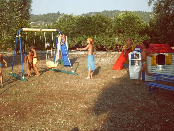 Giardino con scivolo, altalene e bambini che giocano all'aria aperta.
