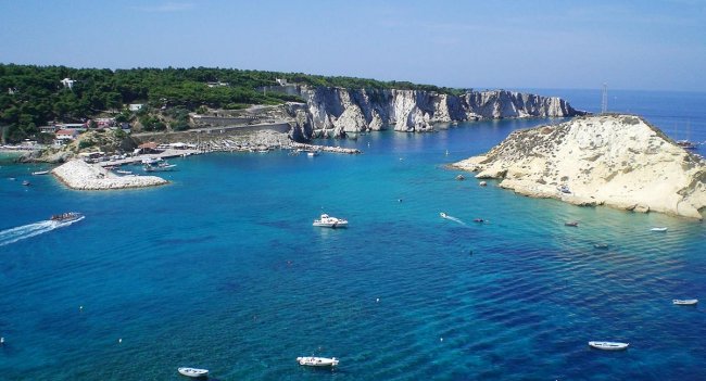 Mare azzurro con barche vicino a scogliere.