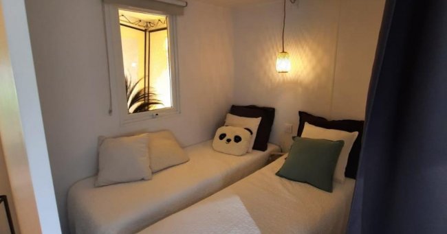 Camera con due letti singoli, cuscino panda, luce soffusa.