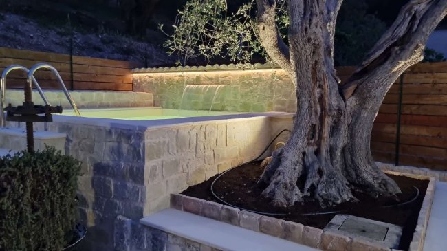 Piscina in pietra con albero illuminato.