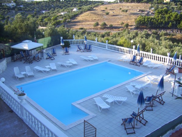 Piscina con lettini bianchi e panorama collinare.