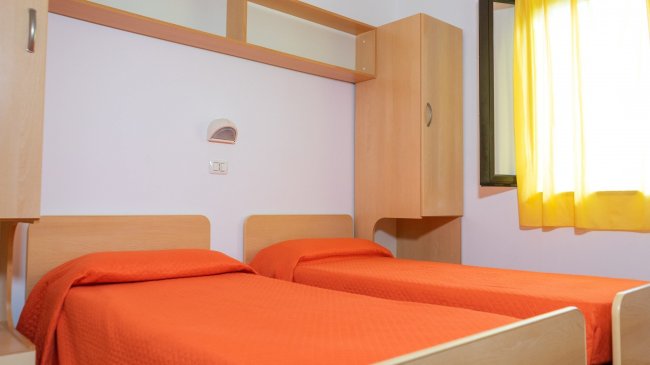 Due letti singoli con copriletto arancione in una stanza luminosa.