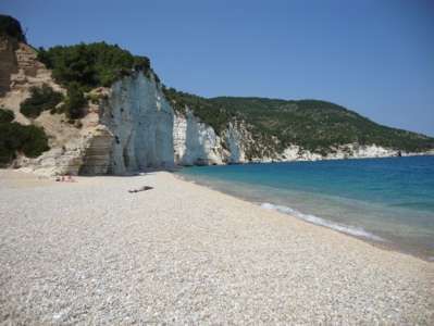 Spiaggia tranquilla con ciottoli bianchi, scogliera bianca e mare blu limpido.