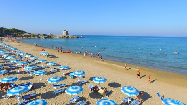 Spiaggia affollata con ombrelloni blu e mare.