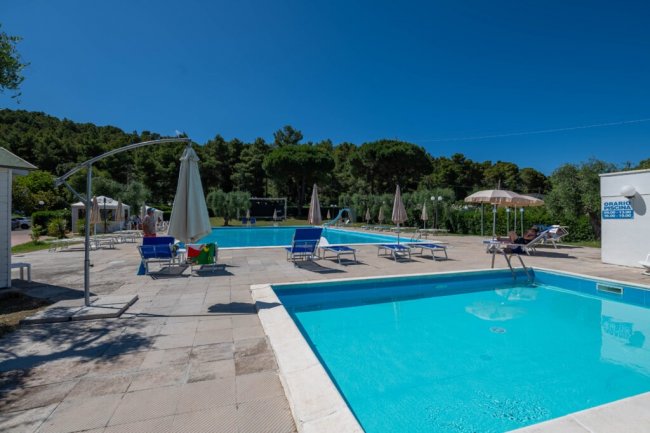 Piscina con sedie a sdraio e ombrelloni, cielo blu.