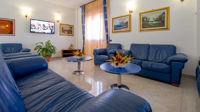 Salotto con divani blu, tavolini e quadri alle pareti.