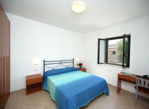Camera con letto matrimoniale, copriletto blu, finestra aperta e scrivania.