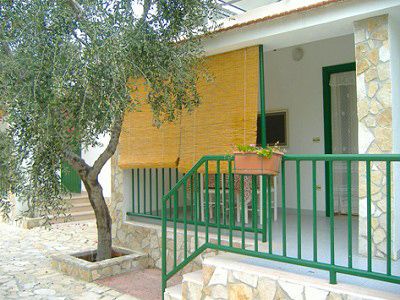 Un piccolo portico con ringhiera verde e tenda di bambù. Un albero adiacente.