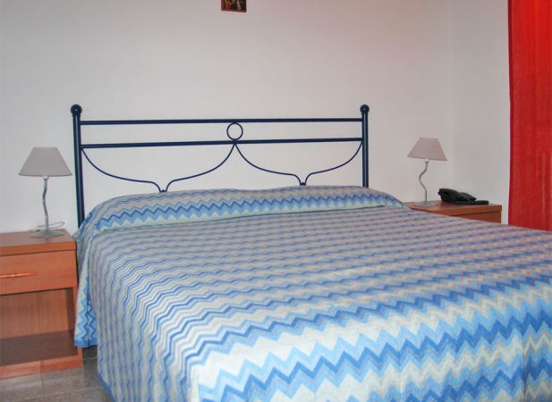 Un letto matrimoniale con copriletto a zigzag blu e verde, tra due comodini con lampade.