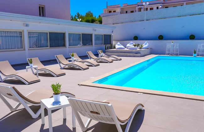 Piscina con sdraio beige e tavolini bianchi.
