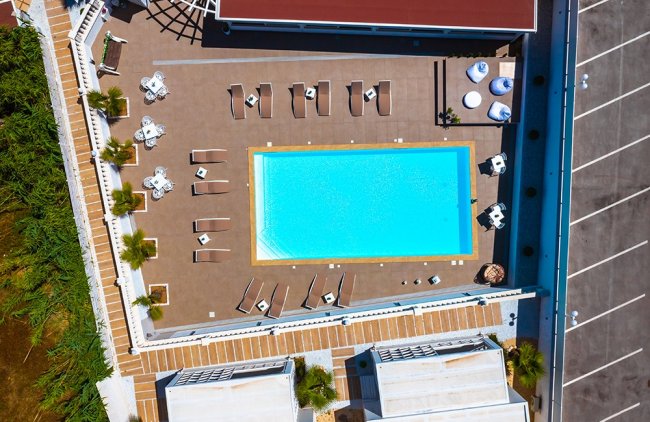 Vista aerea di una piscina con lettini e tavolini.