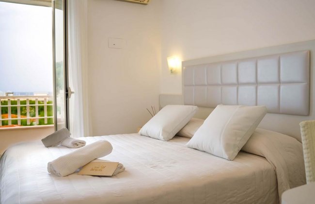 Letto matrimoniale con cuscini bianchi e asciugamani piegati.